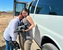 在沙漠中，一名学生抱着摄像机拥抱另一名学生.